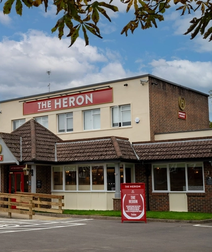 The exterior facade, signage, and car park of The Heron in Havant; with accessible parking spaces near the entrance, and an accessibility ramp leading from the car park to the building.