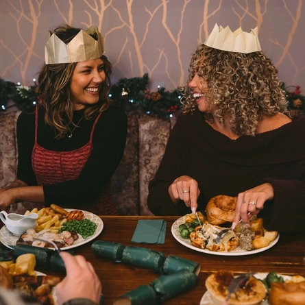 A group of people seated at a festive decorated table  with plated meals and drinks in front of them.