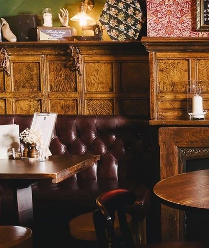 The wood panelled interior restaurant seating area at the Masons Arms, with upholstered booth corner seats, a fireplace, and grape vines carved into the coving around the ceiling.