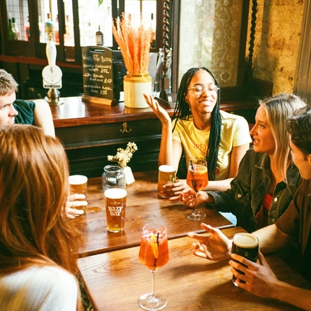 A group off friends sat in the interior restaurant and seating area in a Greene King venue in London with served drinks at the table.