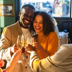 A couple cheersing with a group, with drinks in their hands.