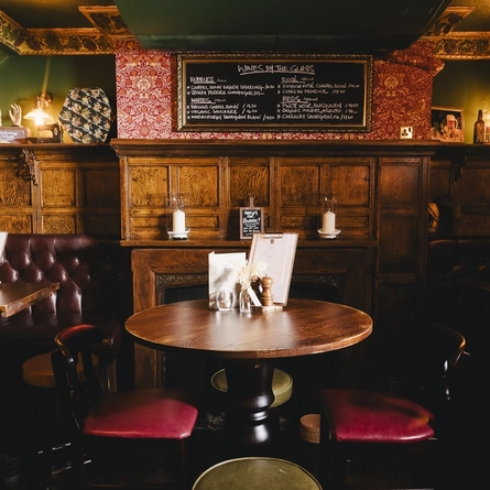 The wood panelled interior restaurant seating area at the Masons Arms, with upholstered booth corner seats, a fireplace, and grape vines carved into the coving around the ceiling.