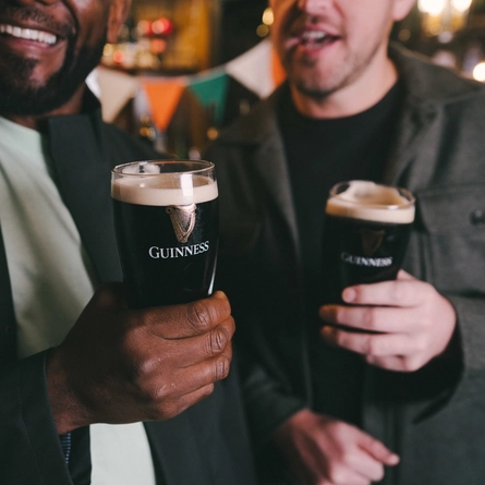 Two people inside a pub, holding glasses of Guinness.