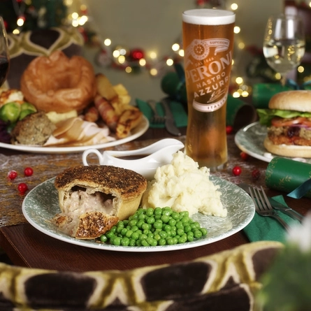 An advertising image focusing on a Festive Turkey Pie dish with various plated Festive Main dishes in the background and a selection of drinks available at a Pub & Carvery venue.