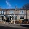 The exterior facade, signage, and seating area of The Horsforth, with wooden picnic tables, shade umbrellas, and strings lights above the seating area.