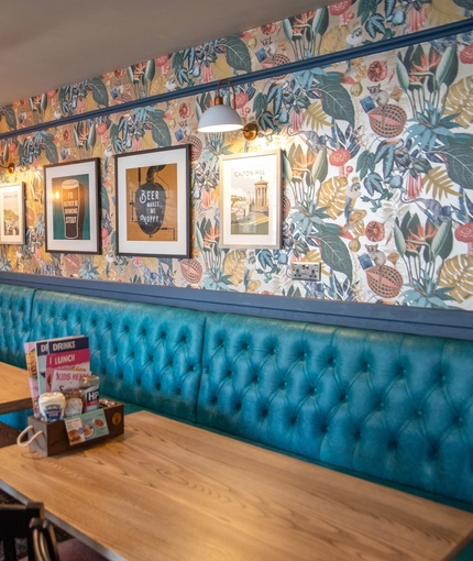 The interior restaurant seating area of The Merlin, with upholstered booth seating, wooden tables, and framed artwork on the wall.