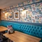 The interior restaurant seating area of The Merlin, with upholstered booth seating, wooden tables, and framed artwork on the wall.