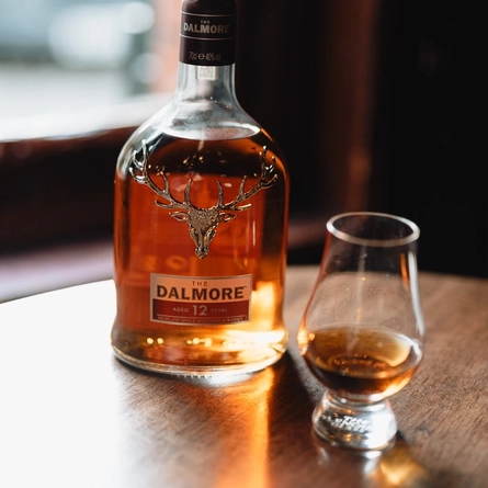 A bottle of The Dalmore Whisky on a table next to a whisky glass.