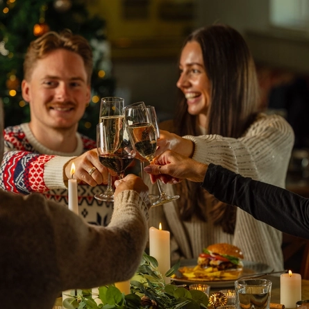 An image of people sat within the interior restaurant seating area with main dishes celebrating with a cheers at a Venture Hotel venue.