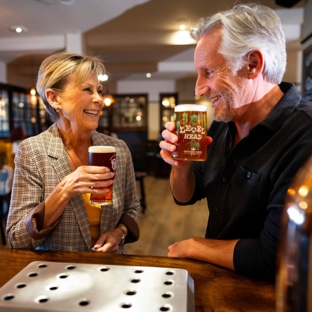 An image of 2 people stood at the interior bar with 2 drinks at a Community Pubs With Food venue.