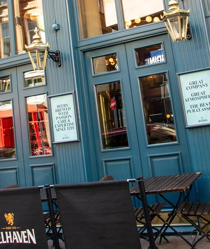 The exterior facade, signage, and seating area at the Rhoderick Dhu in Glasgow; with large golden lanterns hanging on the wall.