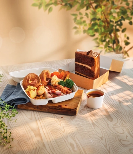 A takeaway box with a carvery inside it, next to a takeaway box with a slice of cake in it.