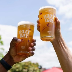 Two hands, each holding a pint of Hazy Day in the air,  with the sky as a backdrop.