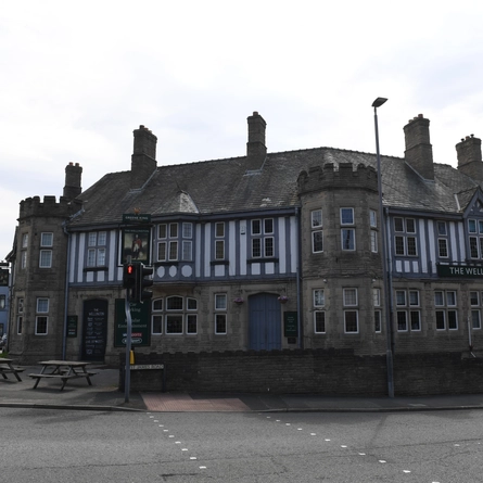 The exterior facade occupying a corner position with venue signage and outdoor seating wooden benches at The Wellington.