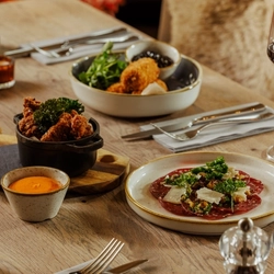 An advertising image of 3 Game Night Starter dishes and a glass of red wine within the interior restaurant and seating area at The Foundry Bell.