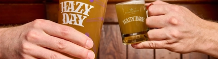 An image of a pint of Hazy Day and a tiny "pint" of Hazy Day advertising taster samples available at some Greene King venues.