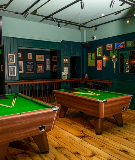 The interior games area at the Lord Raglan, with two pool tables, bar stool seating, and a TV on the wall.