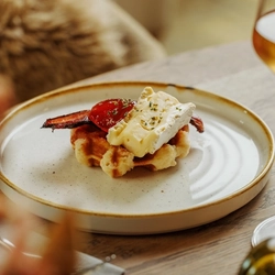 An advertising image of a Cheese Night dish showing a selection of cheeses and a glass of white wine within the interior restaurant and seating area at The Foundry Bell.