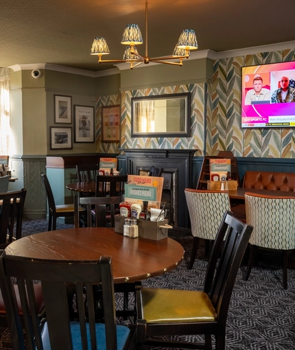 The interior restaurant seating area at The Horsforth in Horsforth, with upholstered booth seats, a TV on the wall, and a fireplace.