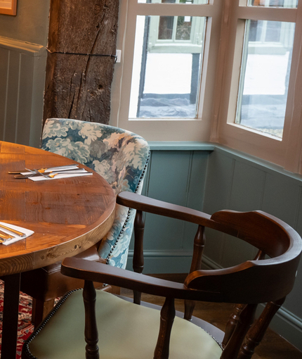The interior restaurant seating area of Ye Olde Swan in Woughton-On-The-Green, with wooden beams, and a fireplace.
