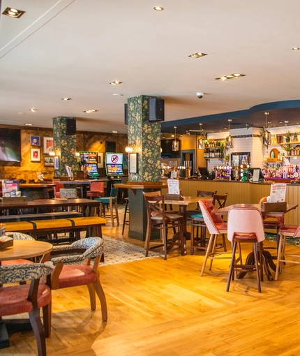 The bar and interior restaurant seating area of The Merlin, with wooden tables and bench seating, TVs on the walls, and pub game machines.