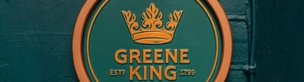A close up view of a circular dark green plaque with the golden yellow Greene King logo in the center, on an exterior wall of The Richmond Arms.