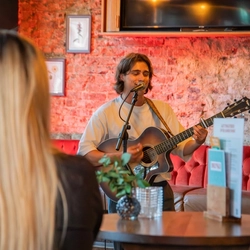 Patrick Ralphson singing into a microphone and playing a guitar,  at a Greene King Summer Pre-awareness event.