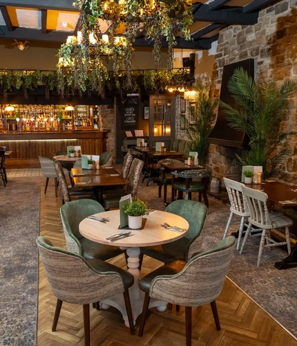 Some tables in The Rockingham Arms restaurant area, with foliage hanging from the windows and lights and the bar in the background.
