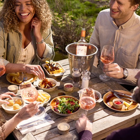 An image of 4 friends sat at a table within the exterior beer garden enjoying glasses of rose wine and a selection of picky bits at a Chef & Brewer venue.