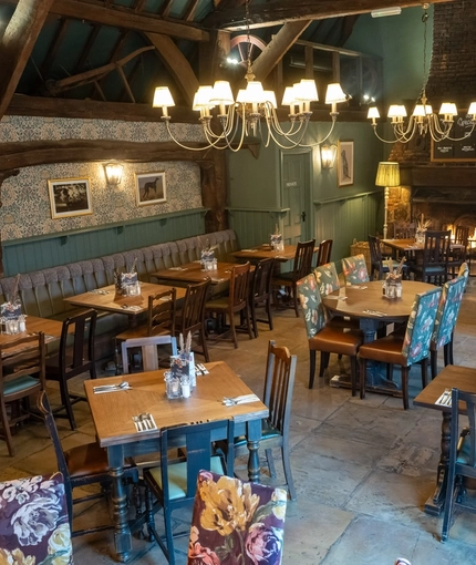 The interior restaurant seating area at The Fox & Hounds in Bursledon, with a vaulted ceiling, wooden beams, stone floor, and large brick fireplace. 