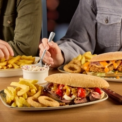 A variety of plated meals on a wooden table.  A hand is holding a fork over one of the plates.