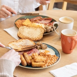 Two women sitting at a table eating from plates of beans, eggs, toast, sausages, mushrooms and hash browns.