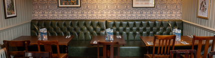 An interior restaurant seating area at The Rising Sun, with a long, upholstered booth seat along one side of the room, wooden flooring, and framed artwork on the walls.