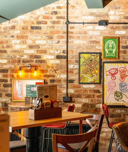 An interior restaurant seating area at The Windmill Inn, with framed artwork, wall lights, and a TV on the exposed brick wall.