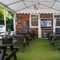 The exterior beer garden seating area under a large gazebo, at The Woolpack Inn in Norwich; with wooden picnic tables, and a TV on the wall.