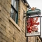 A close up view of the pub sign hanging on the exterior facade of The Red Lion. The sign features a side profile of a rampant red lion beneath the Greene King logo.