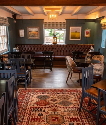The interior restaurant seating area at the Ye Olde Leathern Bottel in Barkham, with wooden flooring, wooden beams, and an upholstered booth seat beneath the windows.