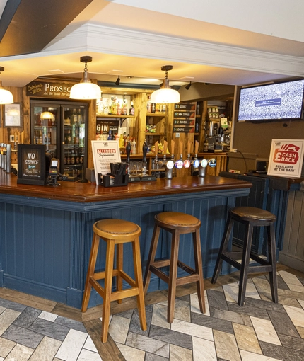 Interior pub area of a pub with stools, a TV and a dartboard.