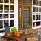 A close up view of one of the wooden tables and wicker-style chairs next to the exterior brick wall of The London Apprentice. Menus and a potted plant sit on the table; a sign on the wall details the history of the pub; and a large beer barrel filled with plants and flowers stands nearby.
