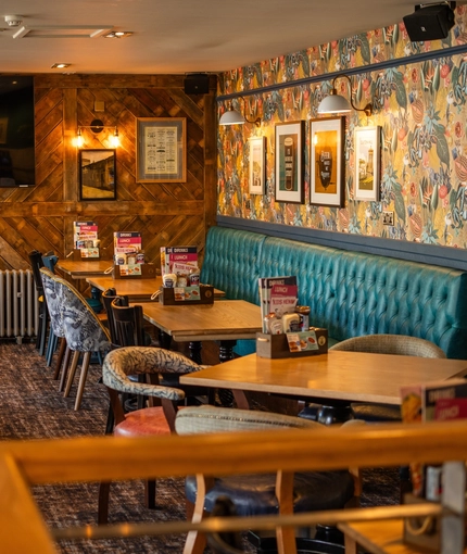 The interior restaurant seating area of The Merlin, with upholstered booth seating, wooden tables, TV and framed artwork on the walls, and a radiator.