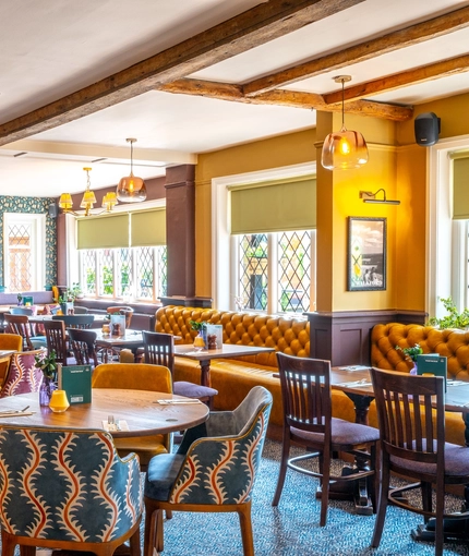 The interior restaurant seating area at The Walkford in Walkford, with a fireplace, upholstered booth seats in front of the leaded windows, and wooden beams on the ceiling.