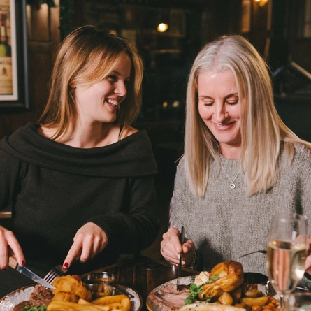 A lifestyle image focusing on 2 customers within a group sat at a table enjoying Mothers Day main dishes and drinks within the interior restaurant seating area at a Heritage venue.