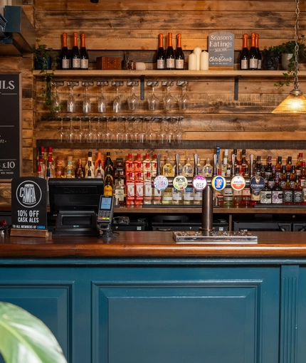 The wood panelled bar inside the Cock & Pye, with bottles of alcohol and glasses on shelves in the background.