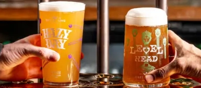 A graphic banner of a pint of Hazy Day and a pint of Level head, both served at the bar being held with a hand.