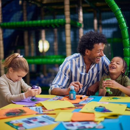 A man participating in crafts with children at a Wacky Warehouse.