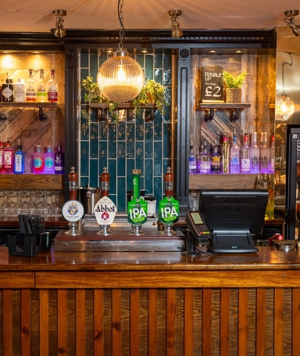 A close up view of the bar and beer taps at the Rudds Arms; with bottles of alcoholic spirits on illuminated shelves behind the counter.