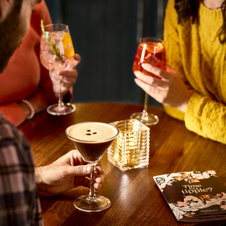 An image of 3 customers with cocktail style drinks sat around a table within the interior seating area at a Chef & Brewer venue.