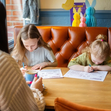 Two children coulouring in activity pages at an indoor table.