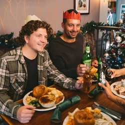 A group of people seated at a festive decorated table  with plated meals and drinks in front of them.