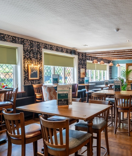 An interior restaurant seating area at The Walkford, with wooden beams on the ceiling, and leaded windows.